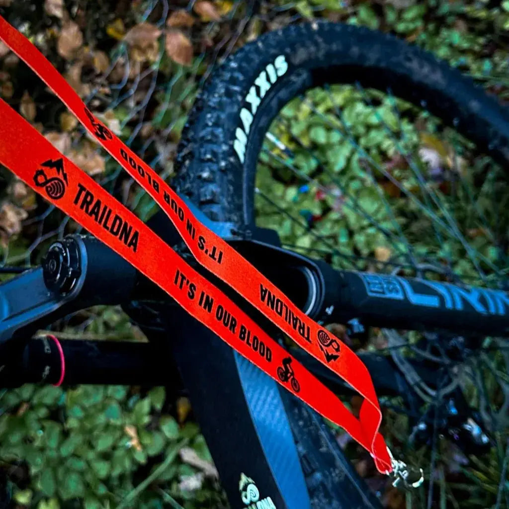 TrailDNA Lanyard orange and black lifestyle shot draped over a mountain bike frame in woodland