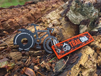 TrailDNA bicycle-shaped multi-tool with orange and black logo keyring on a woodland log.