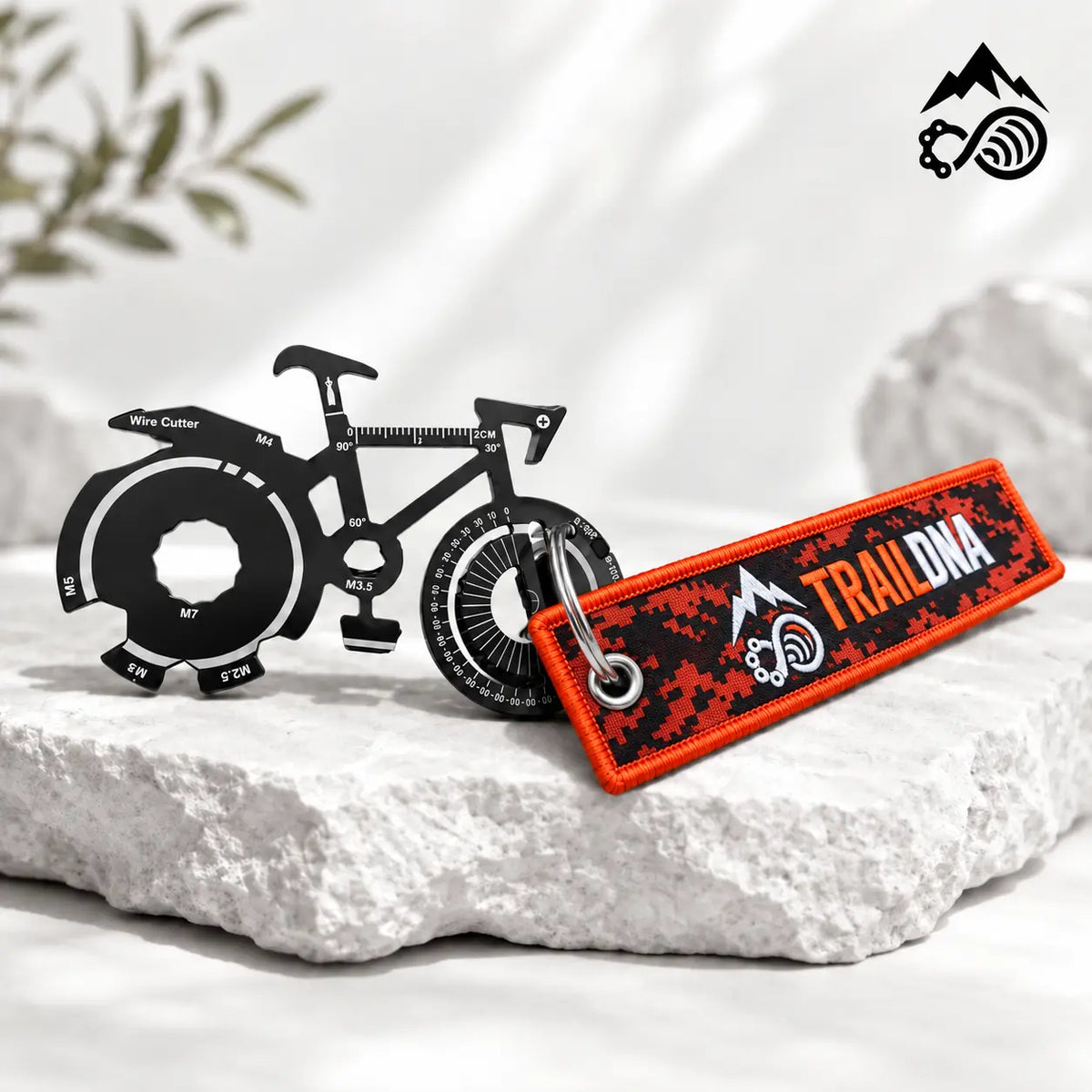 TrailDNA bicycle-shaped multi-tool with orange and black woven keyring on a white stone backdrop.