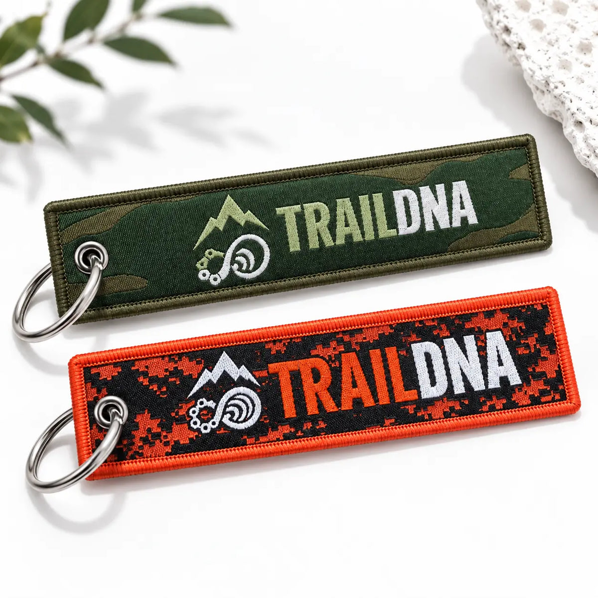 Green and orange TrailDNA woven keyrings showing their front logos on a white background.