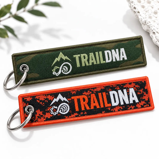 Green and orange TrailDNA woven keyrings showing their front logos on a white background.